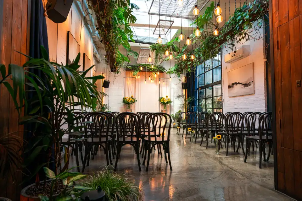 Empty ceremony aisle with bentwood chairs, sunflowers and trailing plants under the Winter Garden skylight at The Hackney