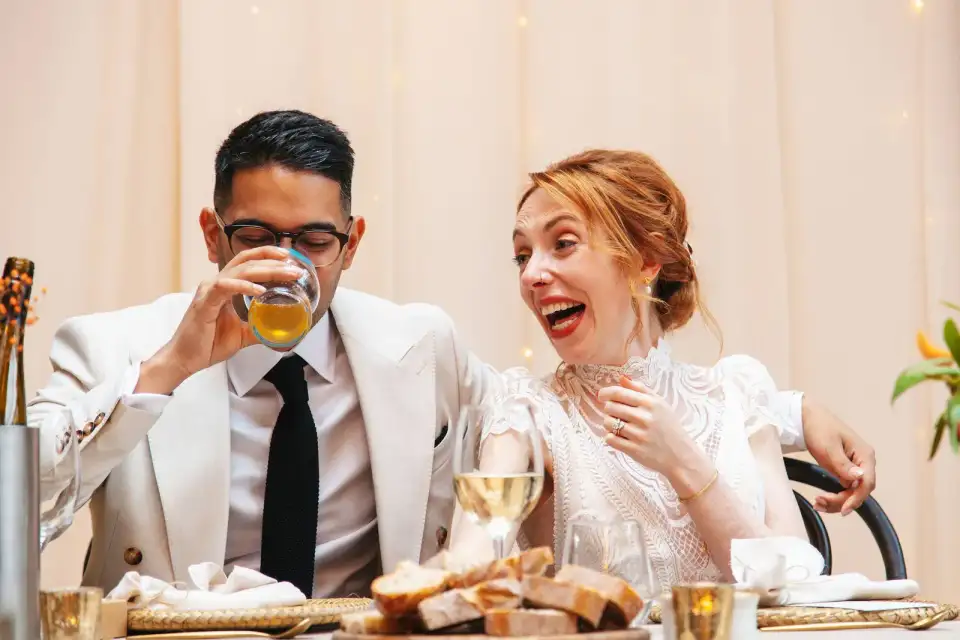 Groom drinking and bride laughing at the top table during the speeches