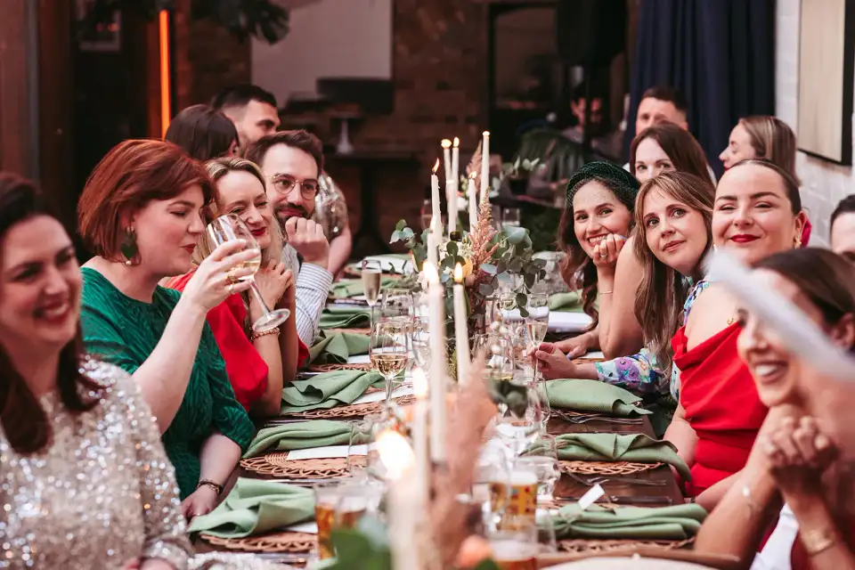 Guests toasting down a long table set with green napkins and tall white candles