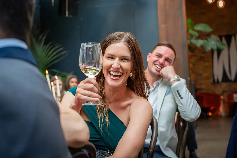 Wedding guest raising a glass of white wine and laughing at the dinner table