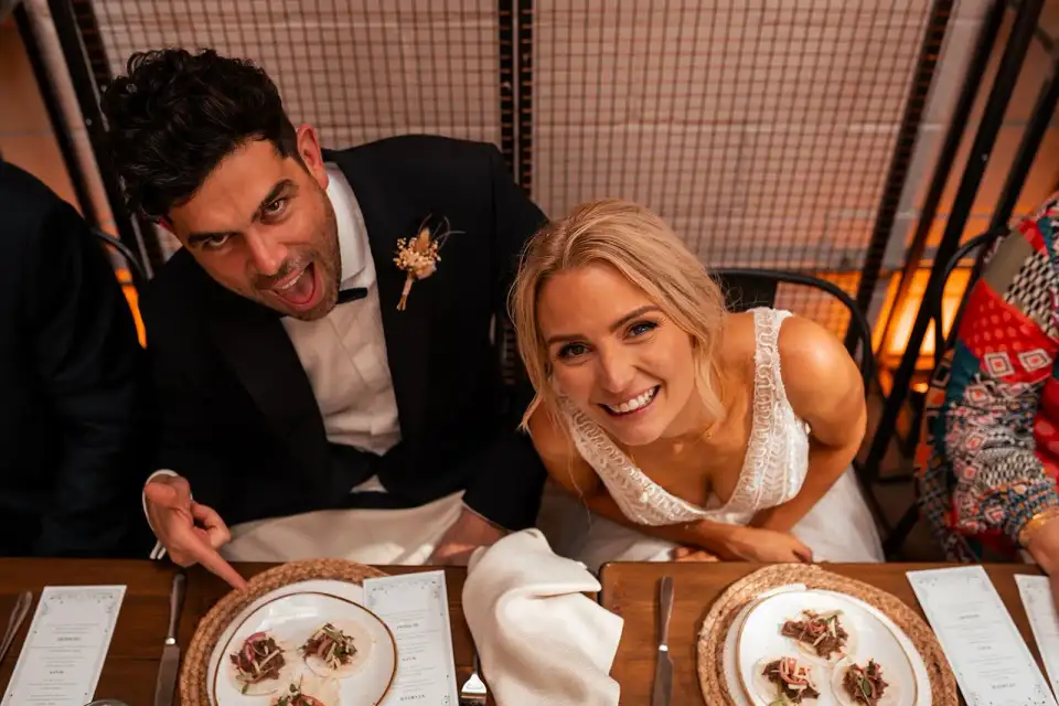 Bride and groom leaning in to the camera over their plates at the wedding breakfast