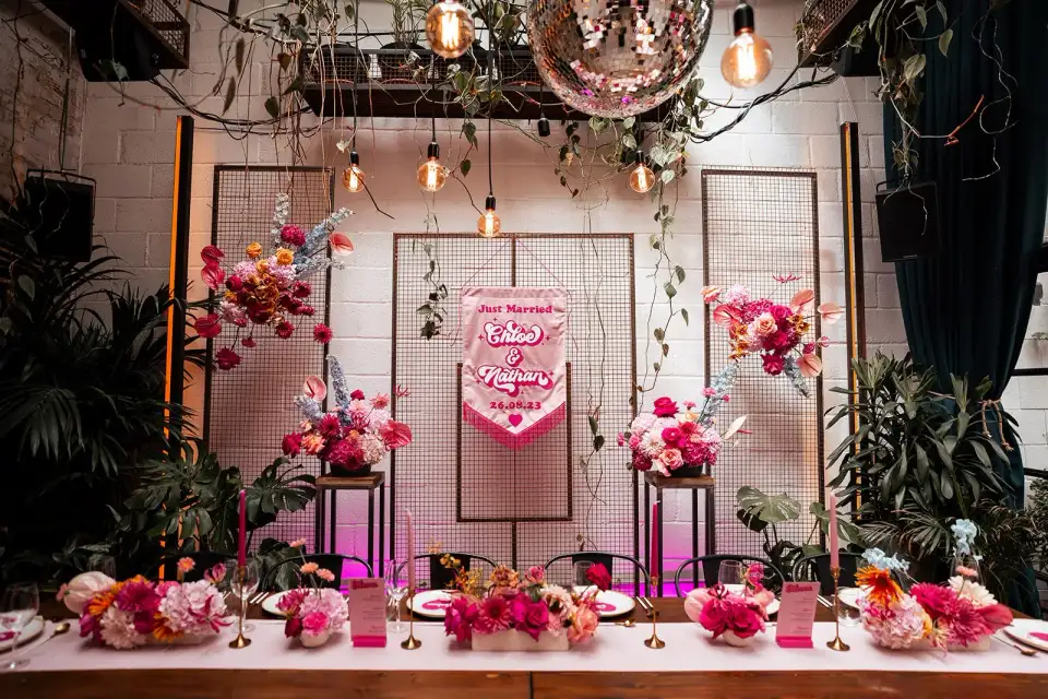 A floral backdrop on the top table, lit with string lights.