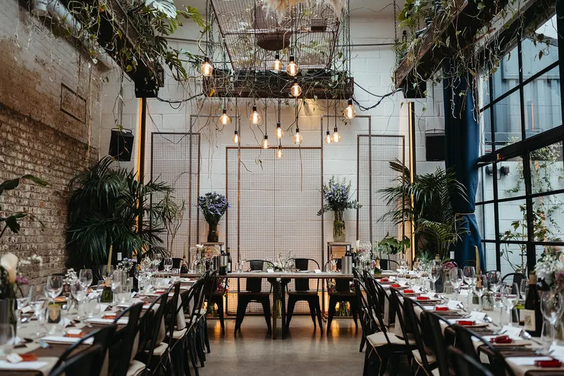 A seated dinner setup in the winter garden at The Hackney with long tables and hanging greenery