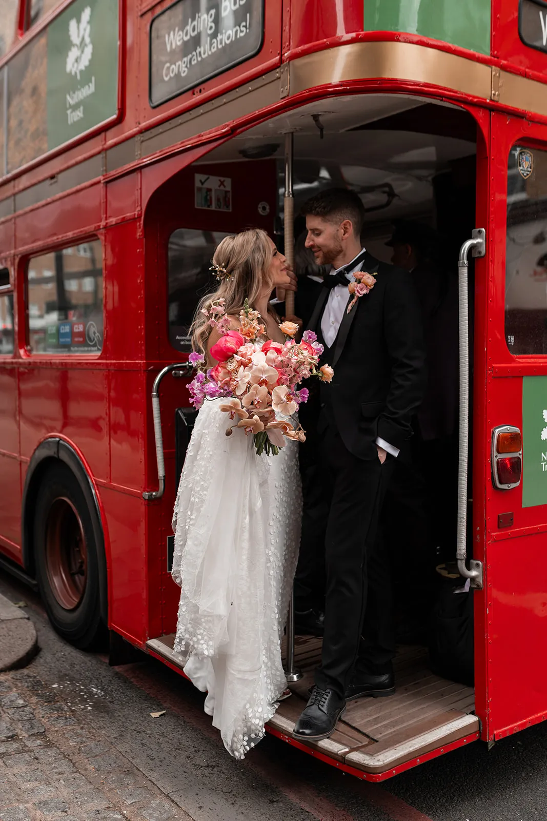 Wedding guests stepping off a red London bus outside The Hackney