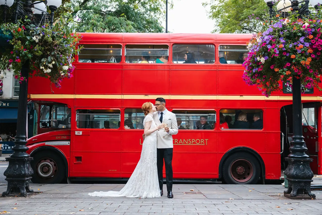 Couple sharing a champagne toast beside the red Routemaster taking their guests on to the reception
